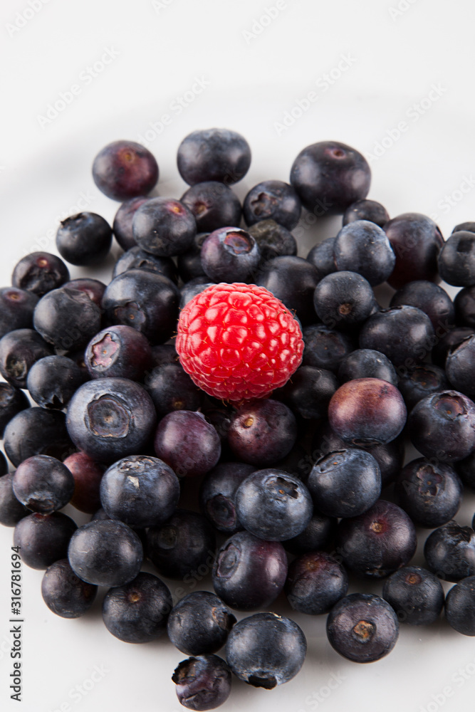 Close-up of raspberry over blueberries against white background Close-up of raspberry over blueberries against white background