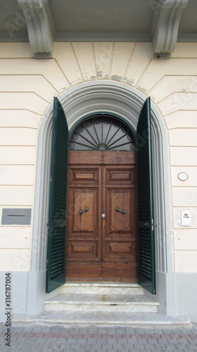 Old Tuscan dark wooden door with green shutters in a white neoclassical style building