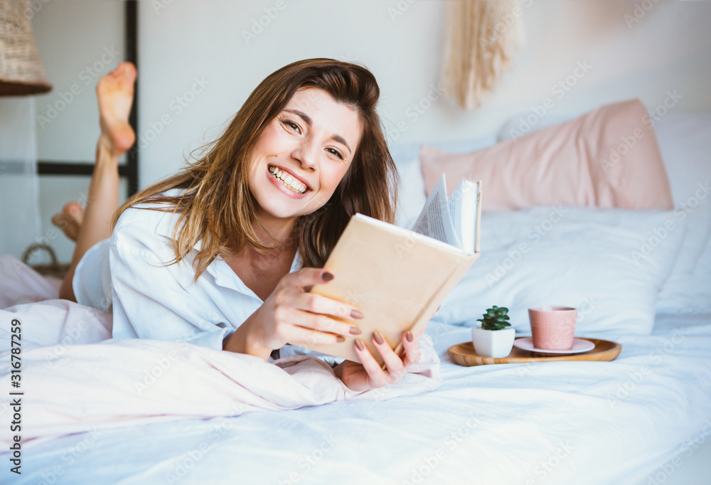 Girl reading a book, drinking coffee or tea, resting in bed. Girl reading a book, drinking coffee or tea, resting in bed.
