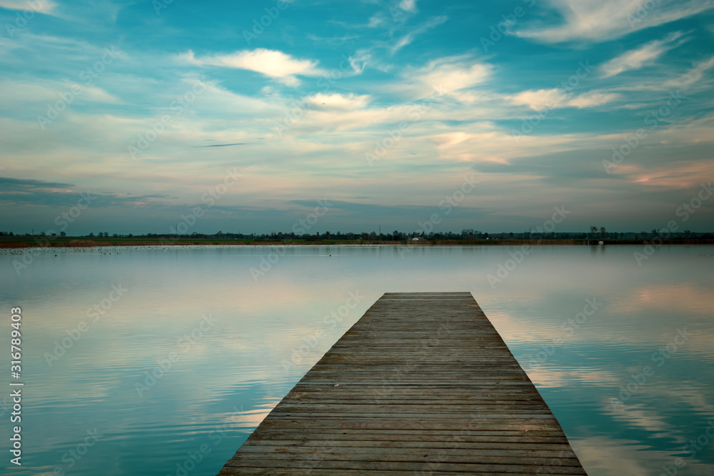 Wooden bridge on the lake, horizon and white clouds on blue sky in Staw, Poland