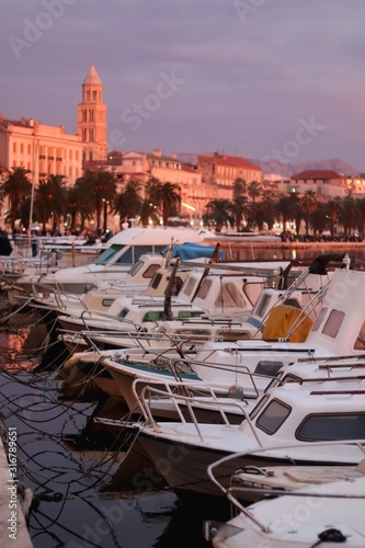 Small fishing boats and historic buildings on Riva promenade in Split, Croatia illuminated by pink sunset light. Selective focus.