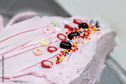 Sweets, chocolate and candies on a pink topping of homemade birthday cake. Chocolate balls, colored candies, soda candies and jellies.