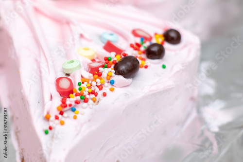Sweets, chocolate and candies on a pink strawberry topping of homemade birthday cake. Chocolate balls, colored candies, soda candies and jellies.