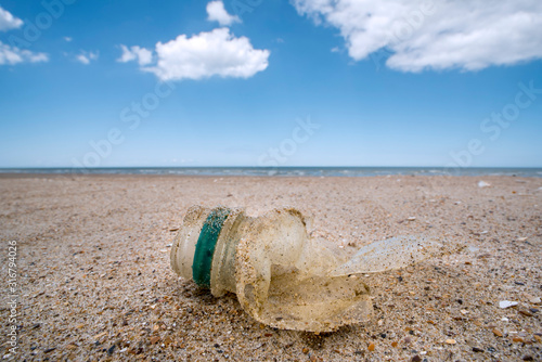 Old partly broken down plastic bottle, non-biodegradable waste washed ashore on sandy beach along the North Sea coast