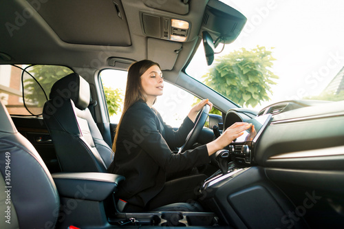 Businesswoman in black suit sits behind the wheel of a premium car and looks the way looking at the monitor of navigation system © sofiko14