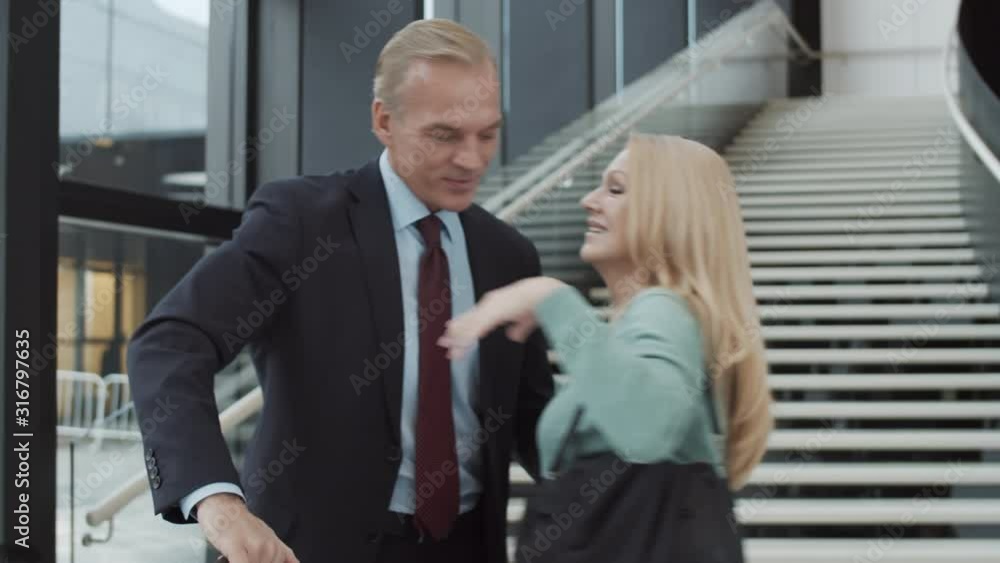 Waist-up tracking shot of loving middle-aged Caucasian wife meeting smiling businessman husband at airport, embracing, kissing, walking away, chatting happily, and people with luggage in background Waist-up tracking shot of loving middle-aged Caucasian wife meeting smiling businessman husband at airport, embracing, kissing, walking away, chatting happily, and people with luggage in background