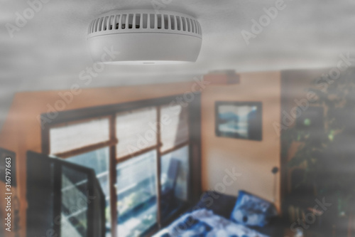 Domestic smoke alarm / battery powered smoke detector on the ceiling in room filled with smoke from fire at home