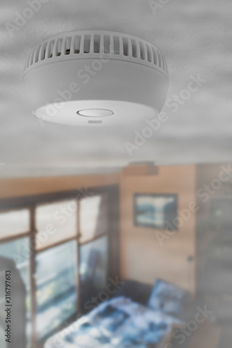 Domestic smoke alarm / battery powered smoke detector on the ceiling in room filled with smoke from fire at home
