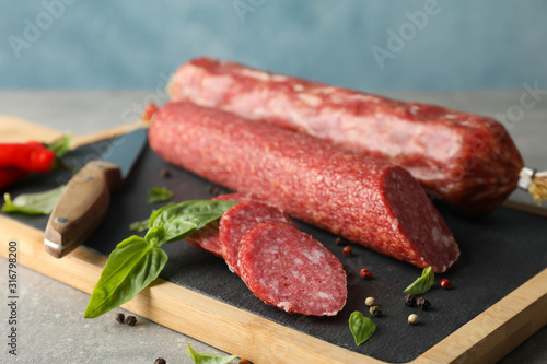 Cutting board with sausage, spice and knife on grey background, close up