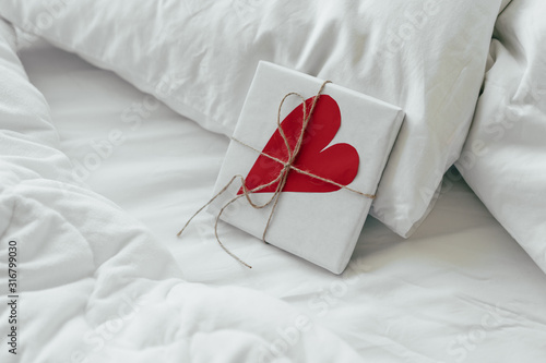 Bild auf Leinwand A gift box with a big paper heart lies in bed early in the morning