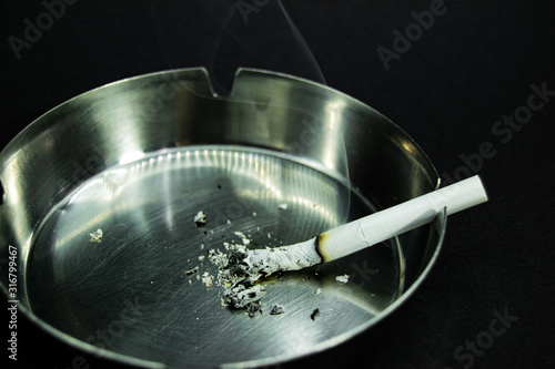 Smoking white cigarette on Ashtray with black background. Unhealthy smoking issues.