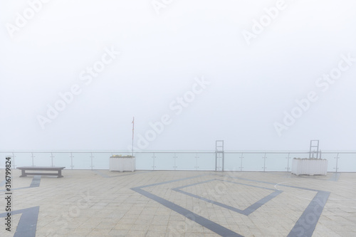 outdoor square with benches, flowerpot and glass fence covered by fog.