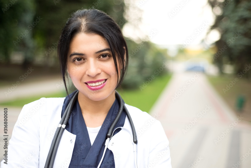 Portrait of a beautiful white, Ecuadorian girl - doctor. In a white coat, with a phonendoscope, smiling. Outdoors Portrait of a beautiful white, Ecuadorian girl - doctor. In a white coat, with a phonendoscope, smiling. Outdoors