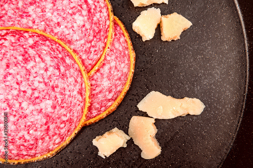 Closeup slice smoked sausage with slices parmesan cheese on black stone plate