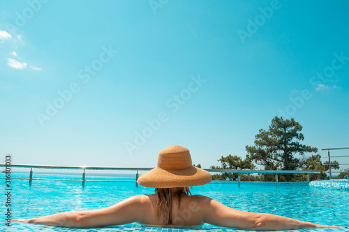 Blonde woman in straw hat in swimming pool with blue endless sky background 