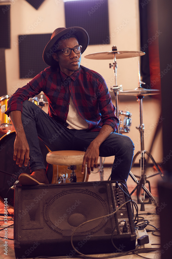 Fototapeta Full length portrait of contemporary African man looking away pensively while posing in music recording studio