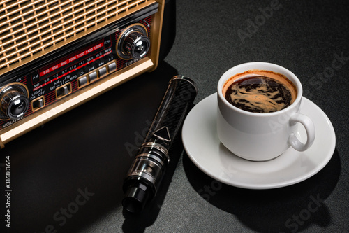 Radio receiver, cup of coffee and electronic cigarette on black surface
