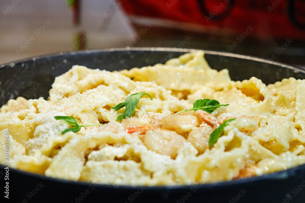 Fried prawns with Italian pasta called mafaldine, Parmesan cheese and herbs in a pan. Fried prawns with Italian pasta called mafaldine, Parmesan cheese and herbs in a pan.