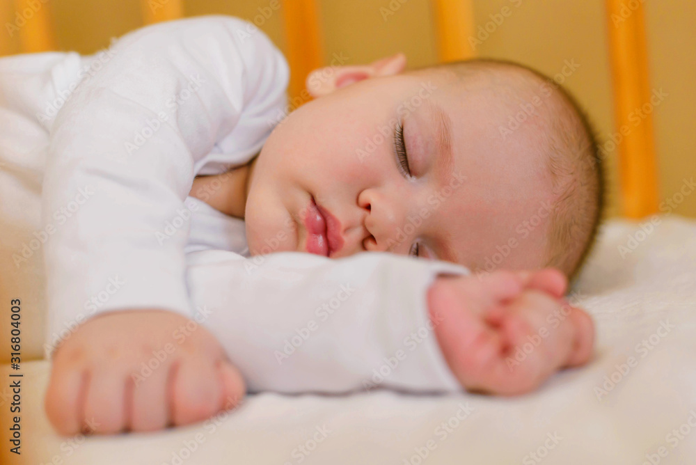 Portrait of a beautiful little boy 5 months old in white clothes, sleeping in his crib. Childhood dreams. Concept of health and children. Selective focus. Portrait of a beautiful little boy 5 months old in white clothes, sleeping in his crib. Childhood dreams. Concept of health and children. Selective focus.
