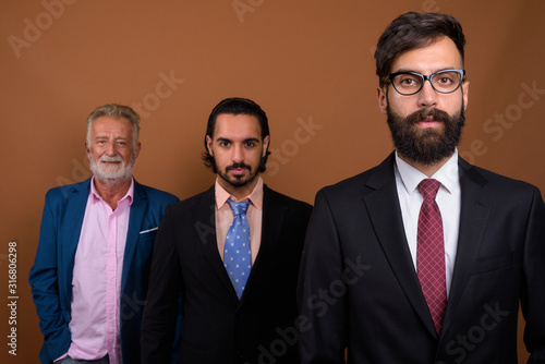 Three multi ethnic bearded businessmen together against brown background