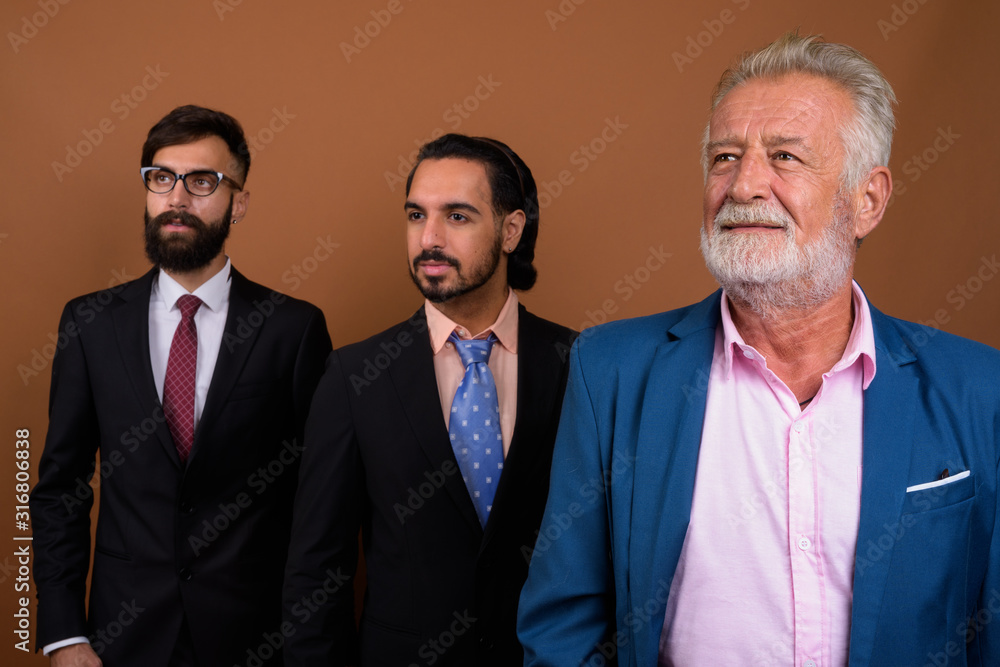 Three multi ethnic bearded businessmen together against brown background Three multi ethnic bearded businessmen together against brown background