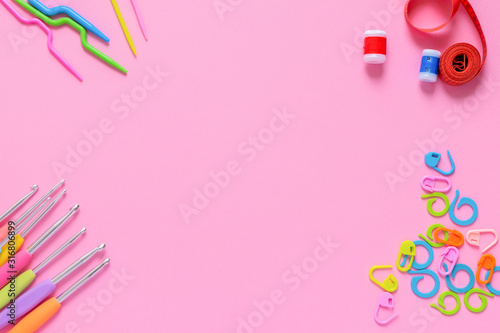 Colorful crocheting and knitting accessories on soft pink background with copy space