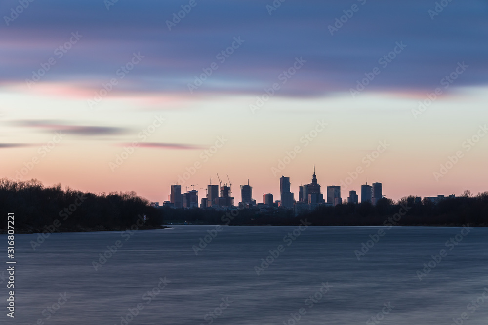 Warsaw skyline with skyscrapers during colorful sunset over the Vistula River.