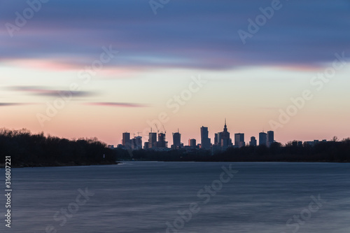 Warsaw skyline with skyscrapers during colorful sunset over the Vistula River.