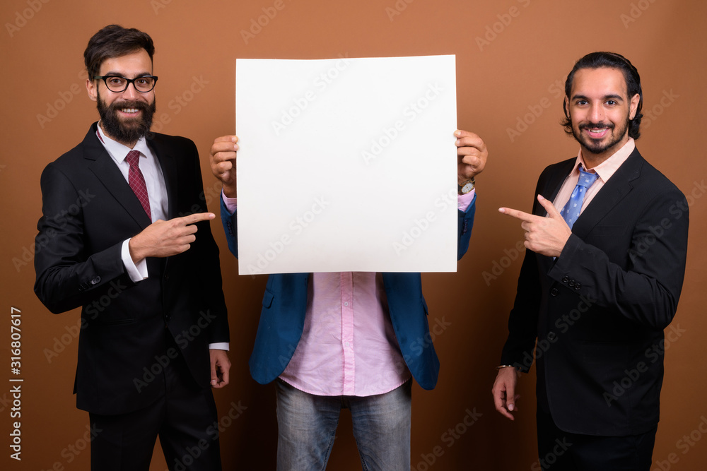 Three multi ethnic bearded businessmen together against brown background Three multi ethnic bearded businessmen together against brown background