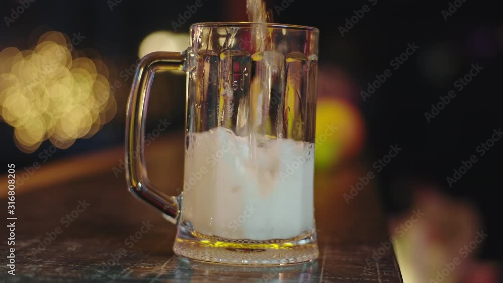 Closeup to the camera in a slow motion cold beer pouring into a glass of beer make bubbles Closeup to the camera in a slow motion cold beer pouring into a glass of beer make bubbles
