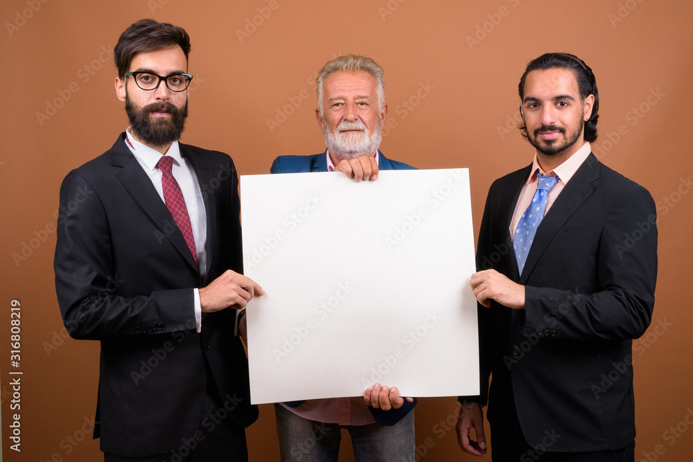 Three multi ethnic bearded businessmen together against brown background Three multi ethnic bearded businessmen together against brown background