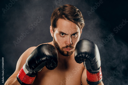 shirtless boxer with gloves on dark background in smoke