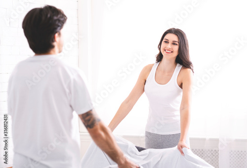 Married couple making bed at bedroom together