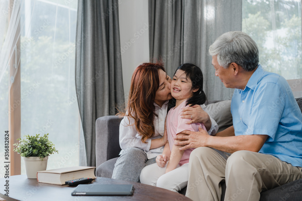 Asian grandparents kiss granddaughter cheek at home. Senior Chinese, old generation, grandfather and grandmother using family time relax with young girl kid lying on sofa in living room concept. Asian grandparents kiss granddaughter cheek at home. Senior Chinese, old generation, grandfather and grandmother using family time relax with young girl kid lying on sofa in living room concept.