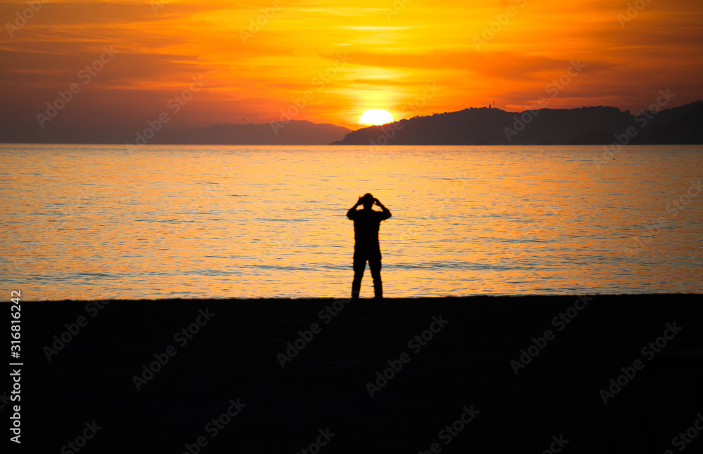 Silhouette of man taking photograph of sunset on beach
