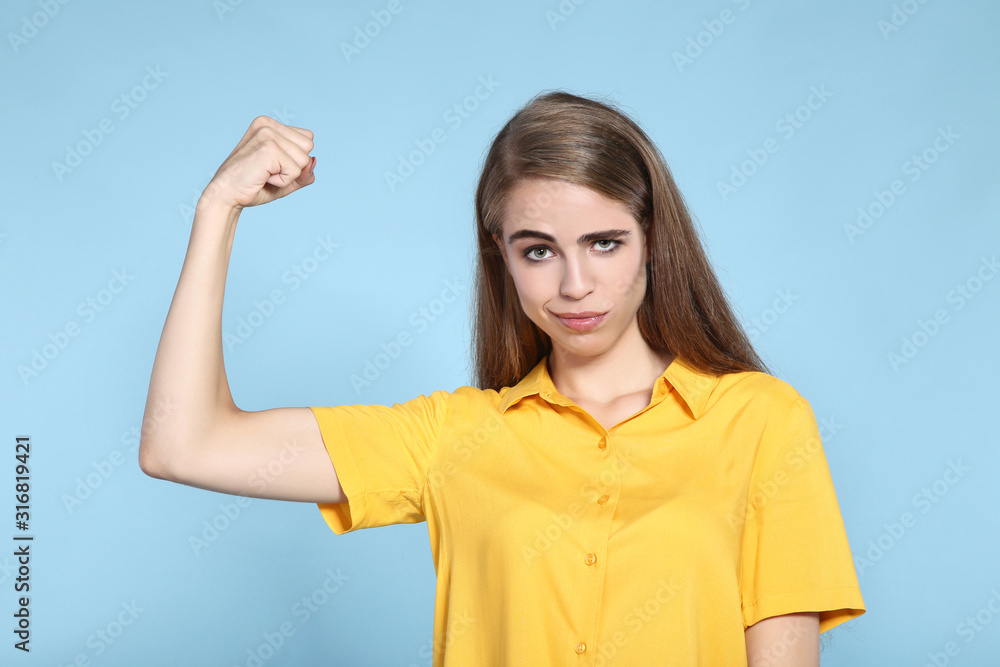 Young beautiful girl showing hand muscles on blue background Young beautiful girl showing hand muscles on blue background