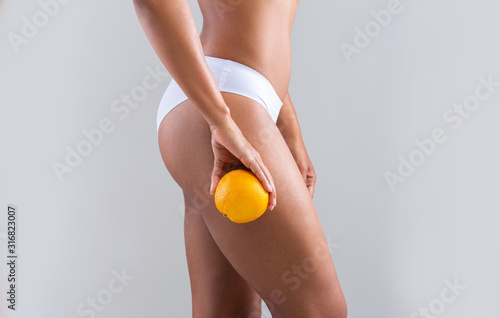 Afro woman holding orange next to her slim sporty legs