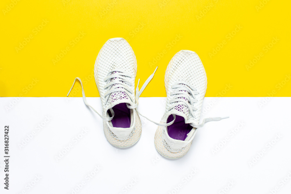 White running shoes on an abstract yellow-white background. Concept of running, training, sport. Banner. Flat lay, top view White running shoes on an abstract yellow-white background. Concept of running, training, sport. Banner. Flat lay, top view