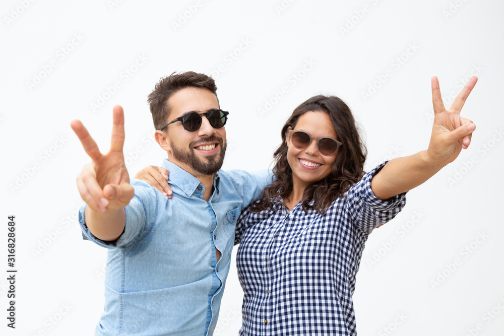 Happy couple in sunglasses showing victory sign. Front view of beautiful cheerful young couple in sunglasses posing together. Happiness concept Happy couple in sunglasses showing victory sign. Front view of beautiful cheerful young couple in sunglasses posing together. Happiness concept