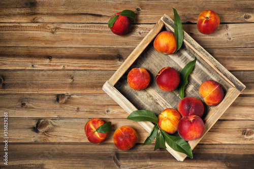 Fresh peaches with green leafs in crate on brown wooden table