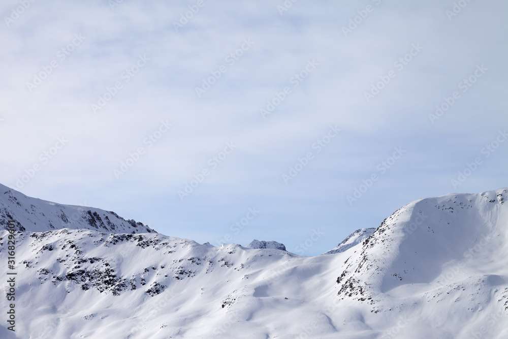 High winter mountains with snowy slopes and sunlit cloudy sky