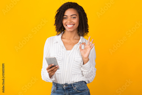 Portrait of smiling black woman using phone showing ok gesture