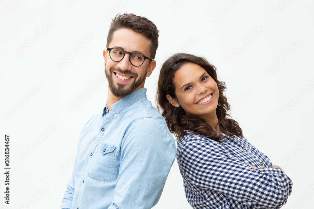 Content man and woman standing back to back. Side view of cheerful young couple standing together and looking at camera on white background. Confidence concept Content man and woman standing back to back. Side view of cheerful young couple standing together and looking at camera on white background. Confidence concept