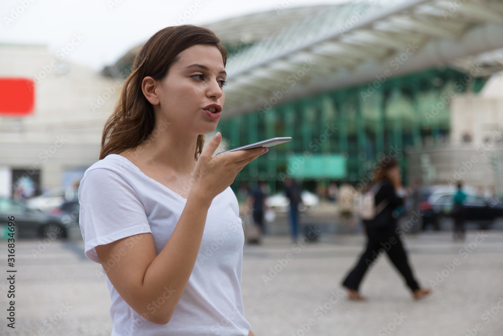 Beautiful woman recording audio message. Focused brunette holding smartphone and taking. Technology concept