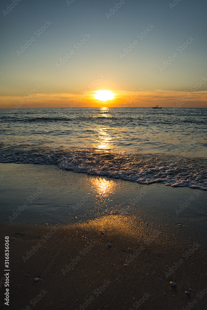 Romantischer Sonnenuntergang, brennender Himmel auf Sunibel Island mit Möven am Himmel und Boot am Horizont