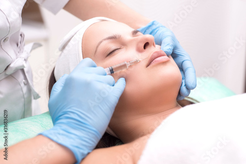 injection into the skin of the face of a young woman, close-up. A cosmetologist with a syringe with a needle introduces a means to remove wrinkles on the face in the lip area.