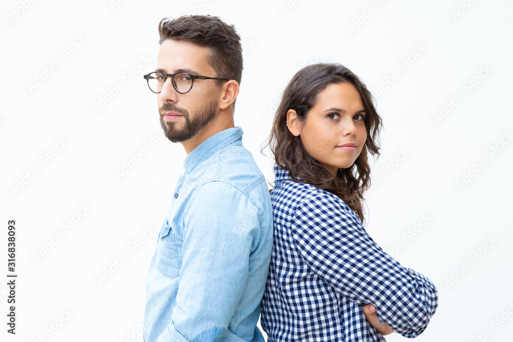 Confident man and woman standing back to back. Side view of serious young couple standing together and looking at camera on white background. Confidence concept Confident man and woman standing back to back. Side view of serious young couple standing together and looking at camera on white background. Confidence concept