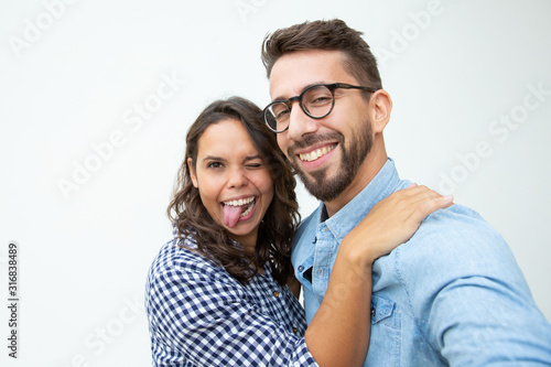 Happy couple grimacing and looking at camera. Cheerful young man and woman fooling around in studio on white background. Friendship concept
