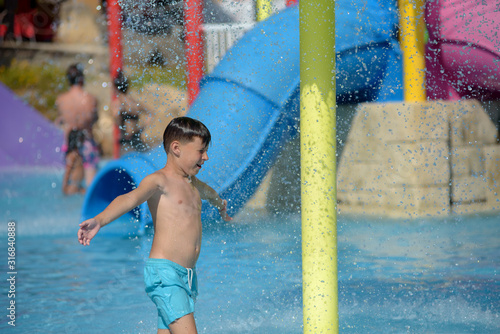 Cute European boy in blue swimming shorts having fun in aqua park he is jumping in pool making lots of splashes. © Artem
