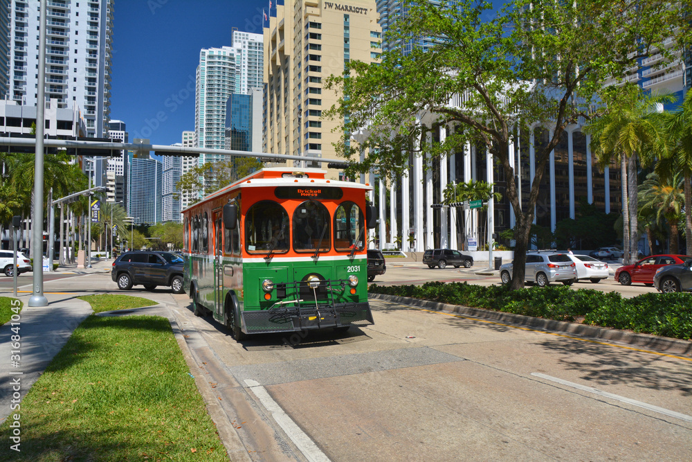 Green trolley goes on Downtown Miami street.
